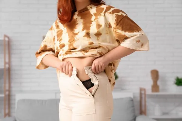 Image of woman trying to do her trousers up after pregnancy weight gain Byfleet